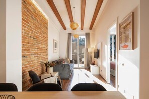 Uma sala de estar moderna com parede de tijolos, vigas de madeira, um sofá, uma mesa de jantar e uma televisão.