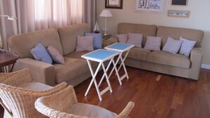 Un salon avec un canapé beige, deux fauteuils en osier, une petite table et une lampe.