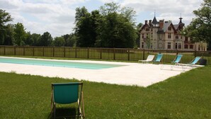 En swimmingpool med liggestole og en stor bygning i baggrunden.