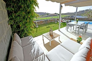 Eine Terrasse mit weißer Gartenmöbeln, einem Tisch und Blick auf einen Pool und Hügel.