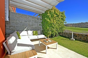 An outdoor patio with a white sofa, a wooden coffee table, and a stone wall. - Salobre Vista Golf 19 (Maspalomas)