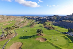 Ein Golfplatz mit freiem Blick auf das Meer, Palmen und einer entfernten Skyline.