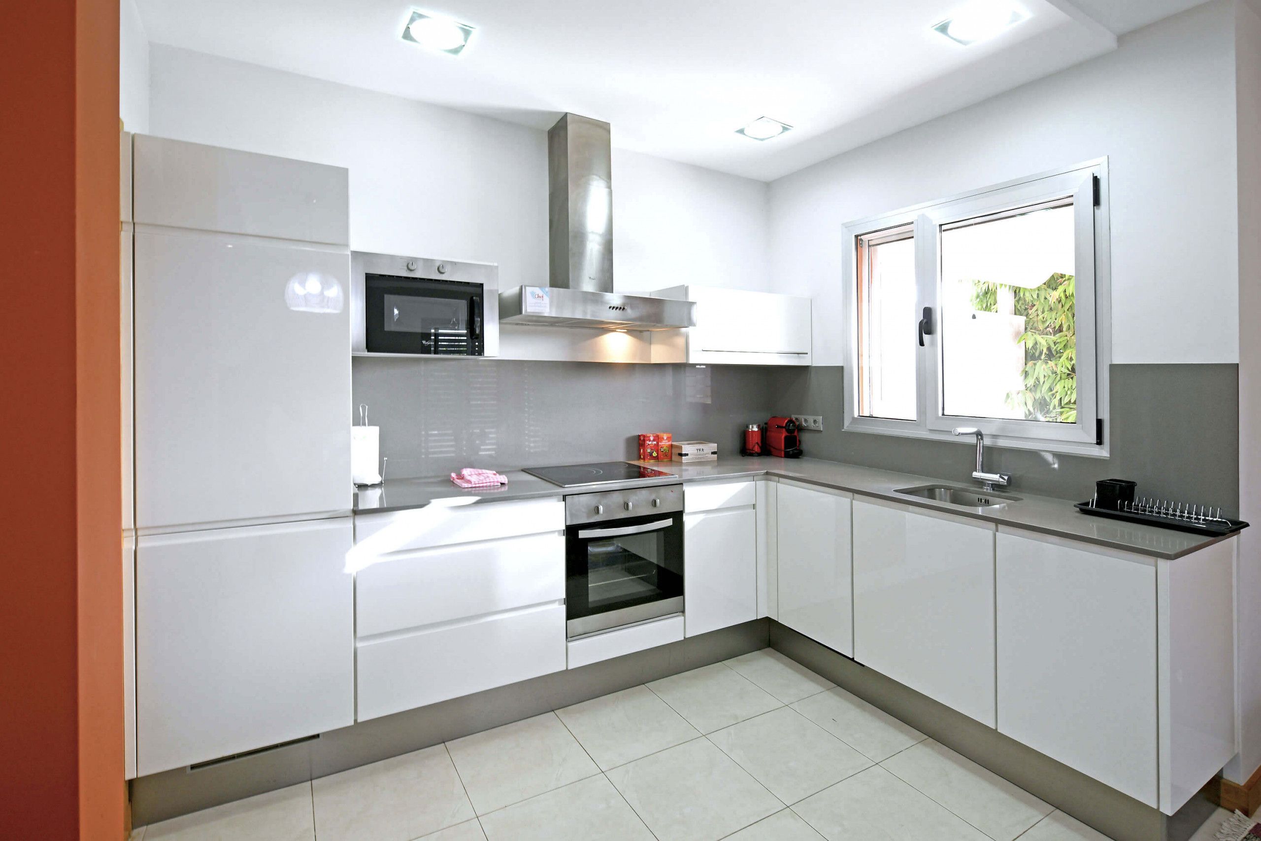 A modern kitchen with white cabinets, stainless steel appliances, and a window providing natural light.