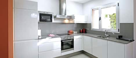 Una cocina moderna con armarios blancos, electrodomésticos de acero inoxidable y un ventanal que proporciona luz natural.