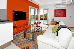 Uma sala de estar moderna com um sofá branco, uma mesa de centro de vidro e uma TV fixada na parede laranja.