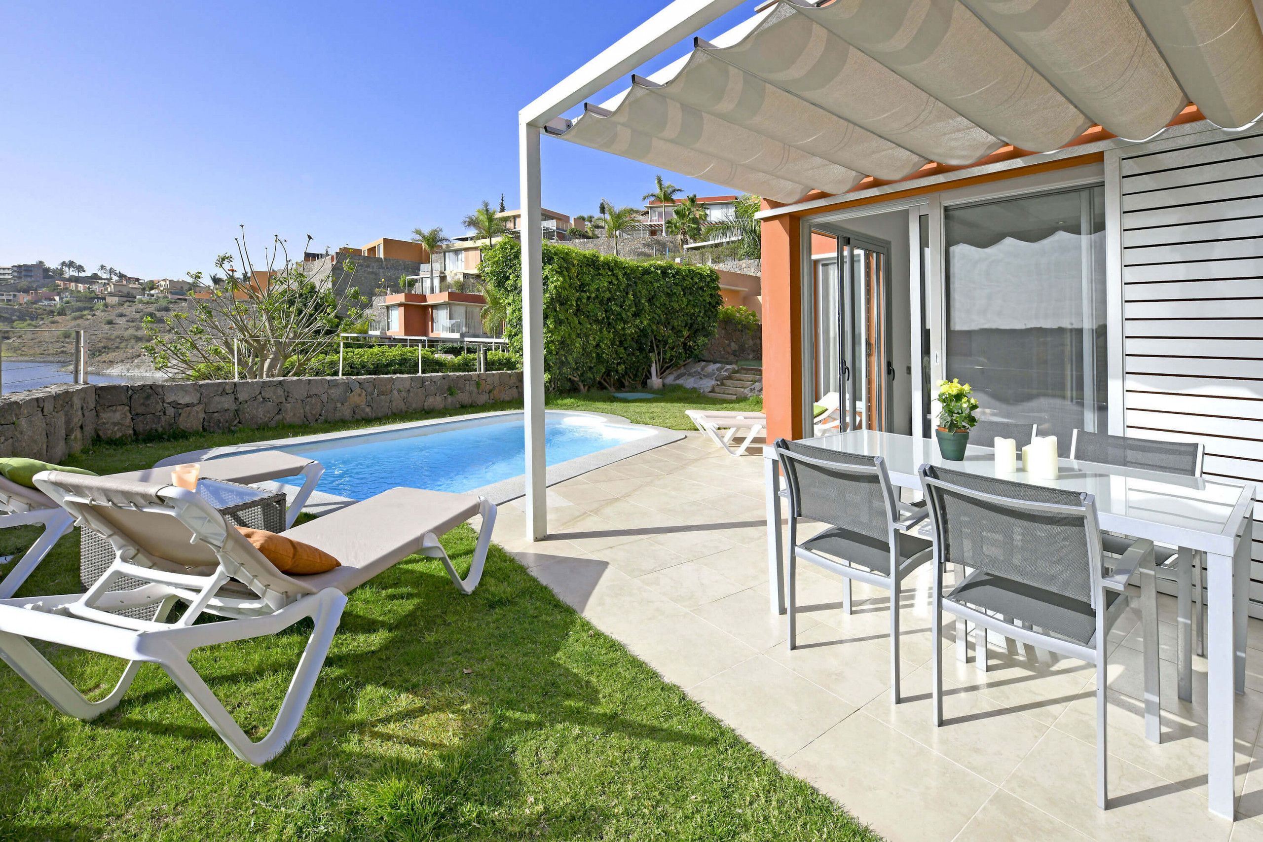 Un espace aménagé au bord de la piscine, avec des chaises longues, une table et une pergola.