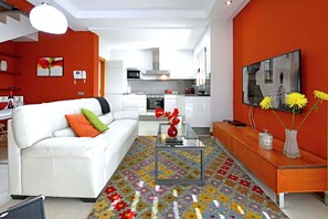 Ein modernes Wohnzimmer mit einem weißen Sofa, einem Glastisch und einem farbenfrohen Teppich mit Muster.