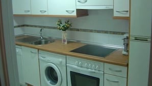 Une cuisine compacte avec des meubles blancs, un lave-linge encastré et un four à micro-ondes.