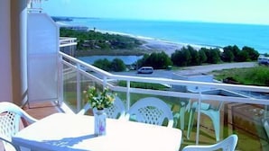 Un balcon avec une table et des chaises, donnant sur une route côtière et l’océan.