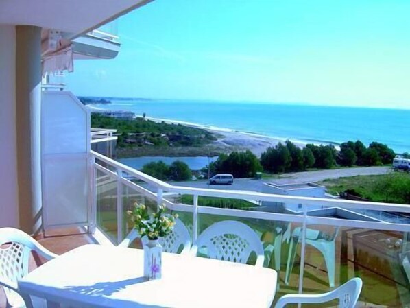 A balcony with a table and chairs, overlooking a coastal road and ocean.
