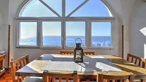 Comedor con una mesa dispuesta para cuatro, un farol sobre la mesa y un amplio ventanal de arco que da al mar.