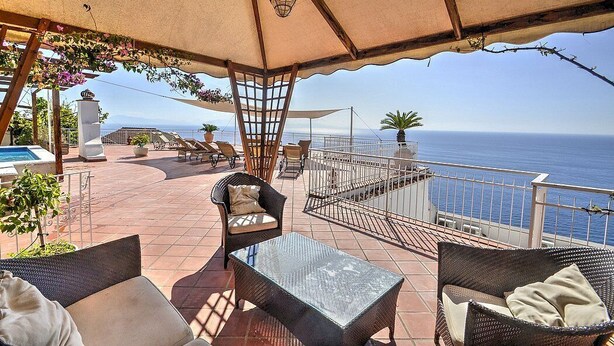 Una terraza con mobiliario de mimbre, una piscina y vistas al mar.