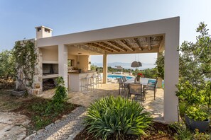 Een modern terras buiten met een zwembad, stenen vloer en een pergola.