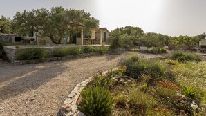A rustic stone house with a gravel driveway, surrounded by lush greenery and flowering plants. - Hacienda NOA/secluded estate/practice golf/enjoy the view and great pool (Grohote, Island of Šolta)