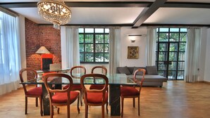 A dining area with a glass table and wooden chairs, a chandelier, and a brick wall. - Loft by KlabHouse w/3BDRM+3BTH+Jacuzzi and Parking near Fond. Prada  (Milano)