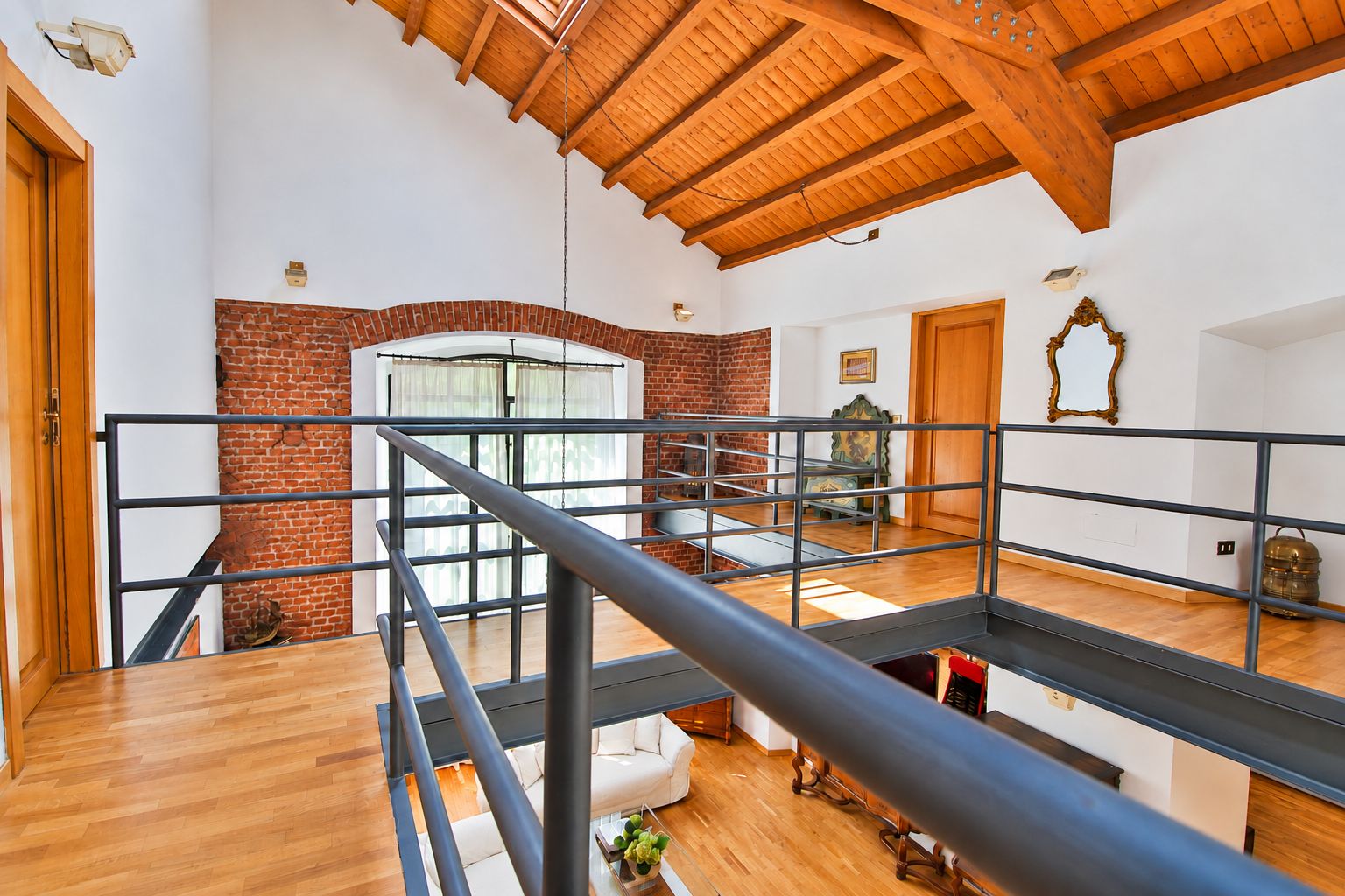 Ein geräumiges Loft mit hohen Decken, freiliegenden Holzbalken, einem Kamin aus Backstein und einem Balkon mit Metallgeländer.
