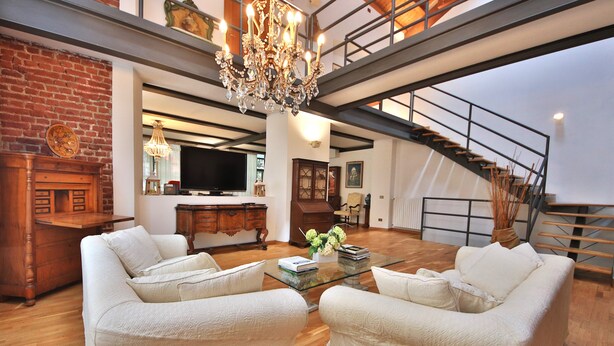 A spacious living room with a high ceiling, a chandelier, a fireplace, a staircase, and a television. - Loft by KlabHouse w/3BDRM+3BTH+Jacuzzi and Parking near Fond. Prada  (Milano)