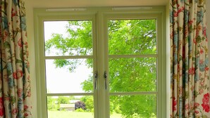 A room with a bed, floral curtains, and a window with a view of greenery. - Peaceful, scenic,cosy cottage near Wells and Frome (Oakhill)