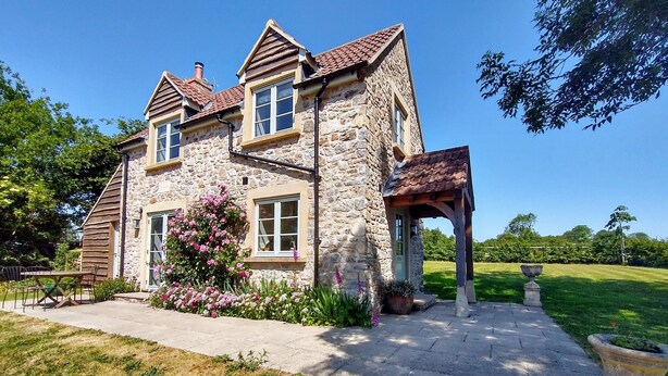 A stone house with a tiled roof, a covered porch, and a garden with flowering plants. - Peaceful, scenic,cosy cottage near Wells and Frome (Oakhill)
