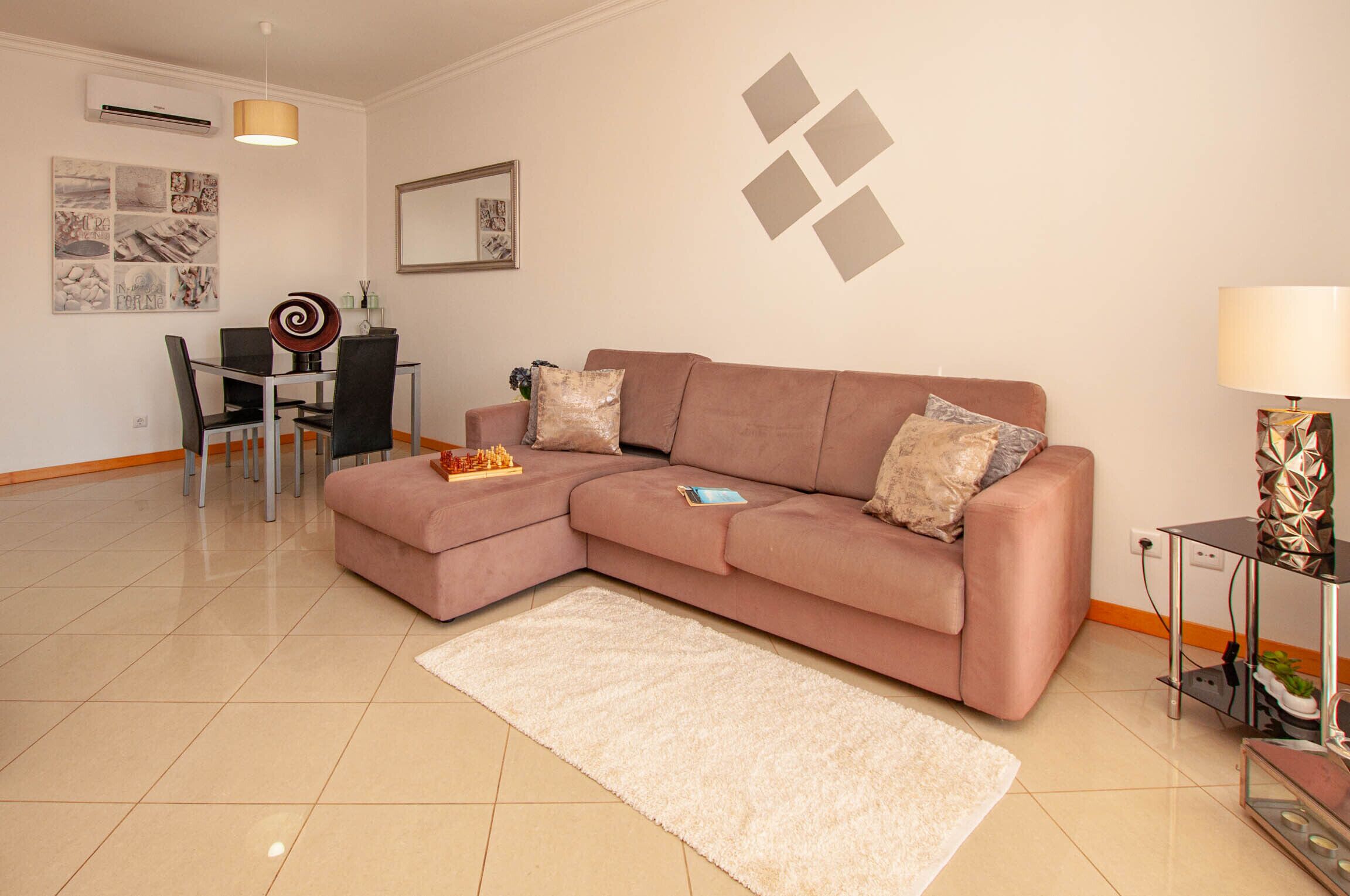 A modern living room with a sectional sofa, a dining table with chairs, a white rug, and a decorative lamp.
