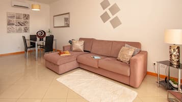 A modern living room with a sectional sofa, a dining table with chairs, a white rug, and a decorative lamp.