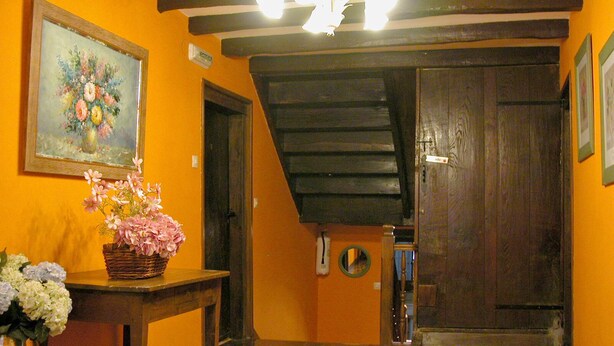 Una habitación con suelo de madera, un cuadro en la pared, una cesta de flores y una puerta que da a otra habitación.