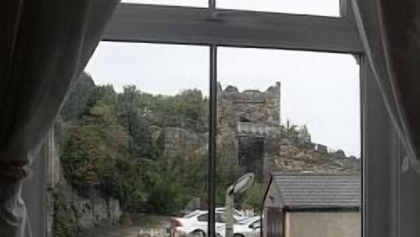A window with curtains, a view of a stone building, and parked cars. - House within Conwy Castle Walls (Conwy)