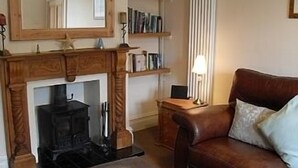A cozy living room with a fireplace, a leather sofa, and wooden shelves with books. - House within Conwy Castle Walls (Conwy)