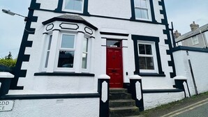 A two-story building with a red door, white walls, and black trim. - House within Conwy Castle Walls (Conwy)