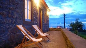 Un bâtiment en pierre avec deux fauteuils confortables à l’extérieur, un mur en pierre et une vue sur le paysage.