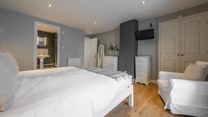 A modern bedroom with a large bed, a white armchair, a dresser, and a wardrobe. - Coxswain's House (4), Wells-next-the-Sea, Norfolk (Wells-next-the-Sea)