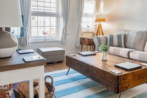 A living room with a wooden coffee table, a sofa, a lamp, and a view of the outside through large windows.
