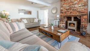A cozy living room with a brick fireplace, a sofa, a coffee table, and a bookshelf. - Coxswain's House (4), Wells-next-the-Sea, Norfolk (Wells-next-the-Sea)
