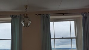 A room with a sofa, a hanging light fixture, and a view of the sea through large windows. - 18th Century Cottage On Waterfront, Panoramic Sea Views, Courtyard Garden (Appledore, nr Bideford)
