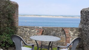 A table and two chairs set against a stone wall overlooking a beach. - 18th Century Cottage On Waterfront, Panoramic Sea Views, Courtyard Garden (Appledore, nr Bideford)