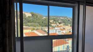 Ein Zimmer mit großem Fenster und Blick auf eine Hügellandschaft mit Gebäuden und Bäumen.