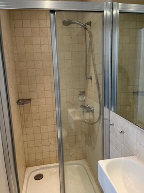 Une cabine de douche fermée par des parois en verre, dotée d’un pommeau de douche à main et d’un robinet fixé au mur.
