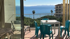 Ein Balkon mit Tisch und Stühlen, Blick auf das Meer und ein Gebäude im Hintergrund.
