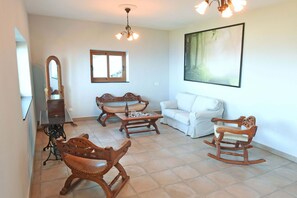 A living room with a wooden rocking chair, a white sofa, a wooden coffee table, and a large painting on the wall. - Villa Vista Mar en Tijarafe (Tijarafe)