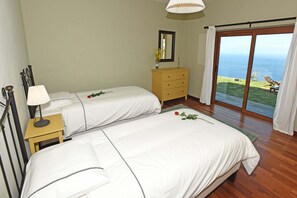 A bedroom with two beds, a nightstand, a dresser, and a large window with a view of the ocean. - Villa Vista Mar en Tijarafe (Tijarafe)