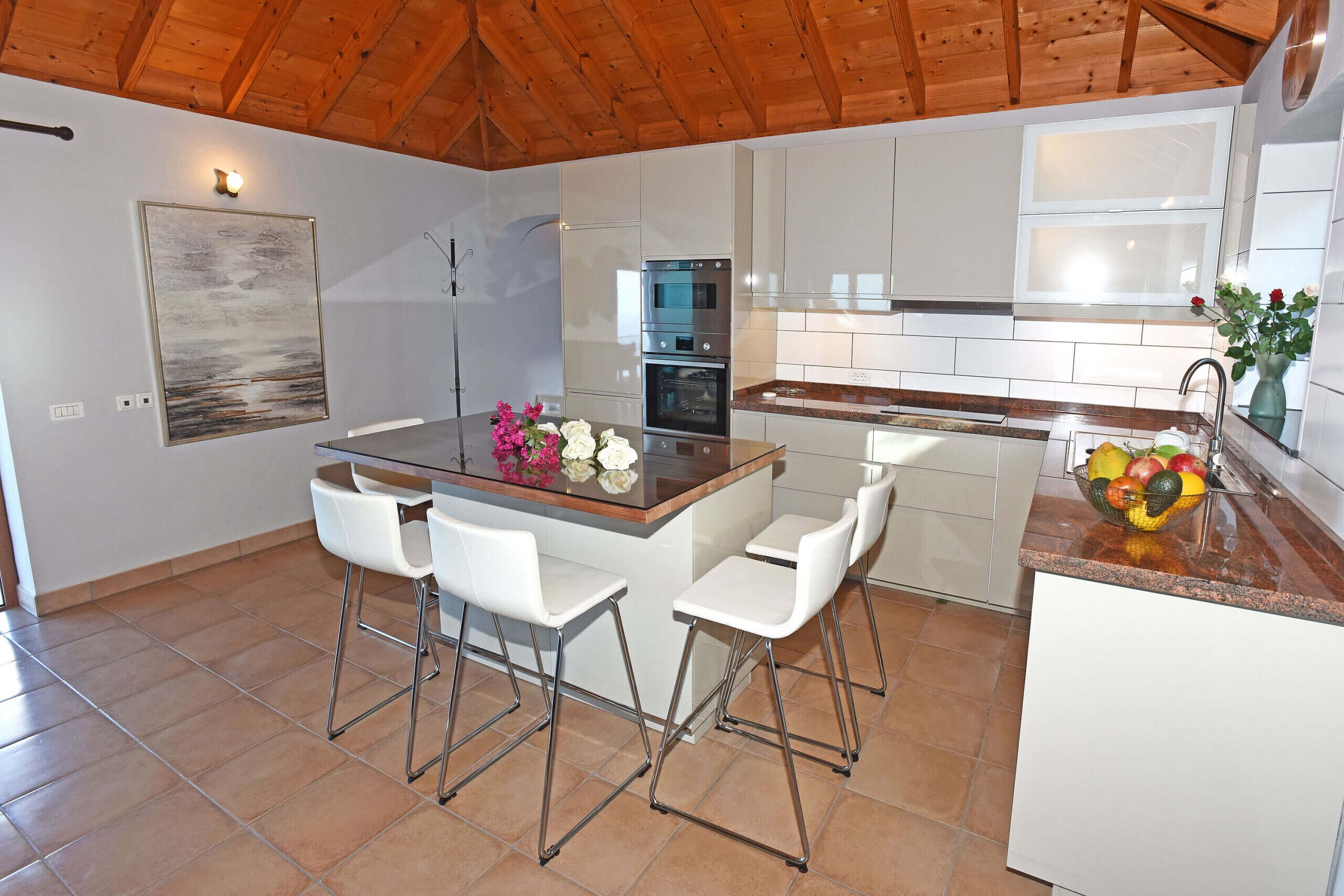 Een moderne keuken met een centraal eiland, krukken, roestvrijstalen apparatuur en een betegelde vloer.