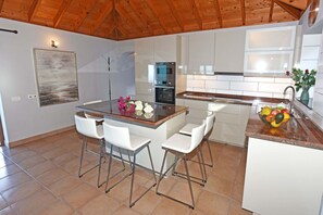 A modern kitchen with a central island, bar stools, stainless steel appliances, and a tiled floor. - Villa Vista Mar en Tijarafe (Tijarafe)