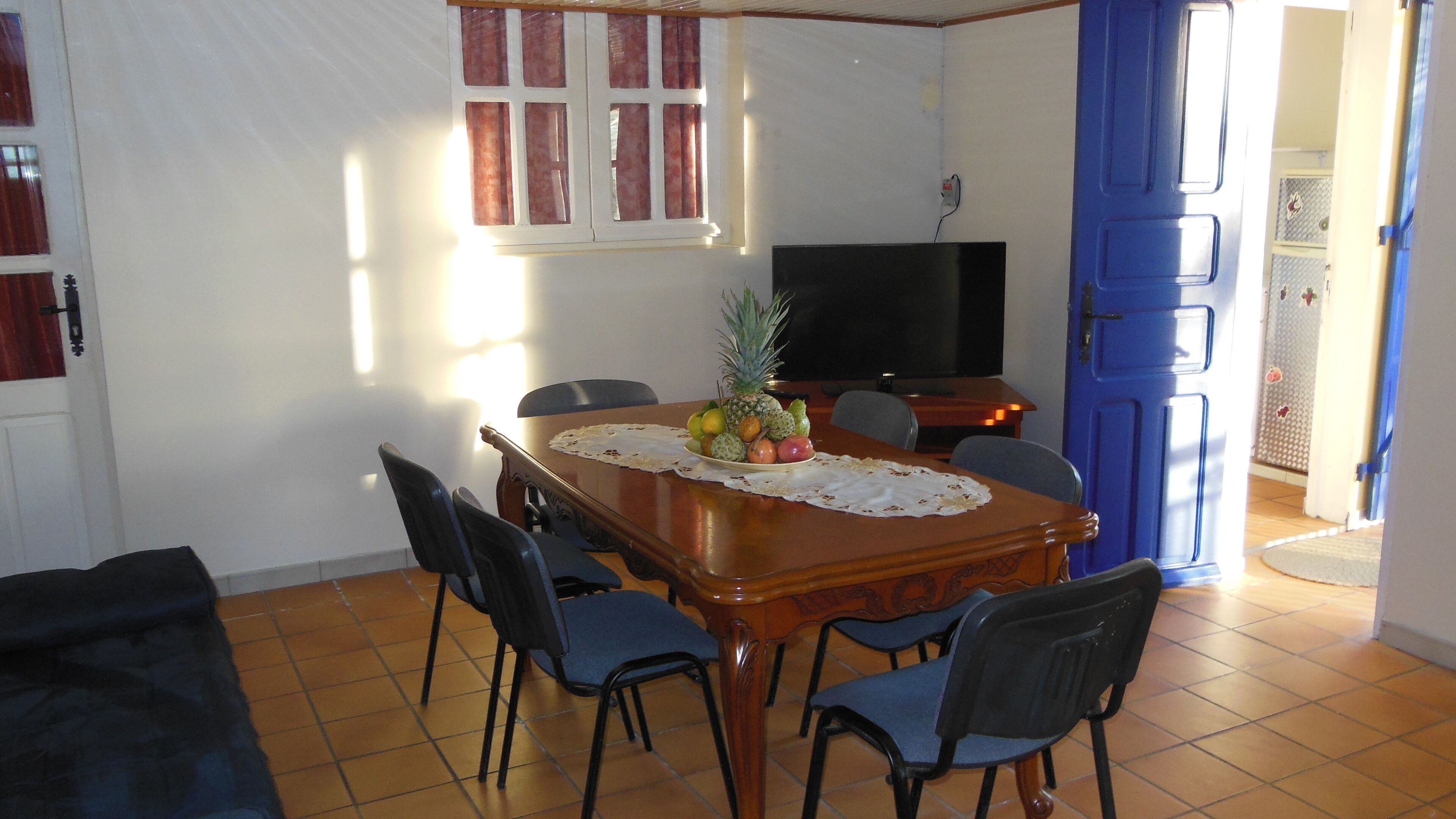 A dining area with a wooden table, chairs, a television, and a blue door.