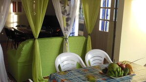 Zona pranzo con tavolo apparecchiato per due, sedie, un cesto di frutta e vista all'esterno da una finestra.