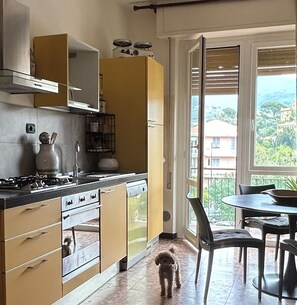 A kitchen with a stove, cabinets, and a dining area with chairs and a table. - THREE-ROOM APARTMENT La Formica Azzurra, terrace overlooking hills, yes pets, near center  (Lavagna)