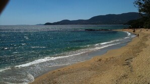 Ein Strand mit klarem, blauem Wasser, sandigem Ufer und fernen Bergen.