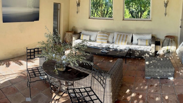 Eine sonnendurchflutete Terrasse mit einer Couch, Korbmöbeln und einem Tisch.