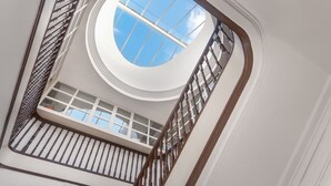 Une lucarne circulaire offrant une vue sur le ciel, un escalier en bois et une rambarde blanche.