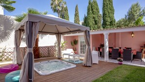 A covered outdoor area with a hot tub, seating, and a patio table.
