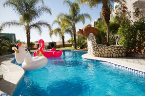 A swimming pool with inflatable swan and flamingo floats, surrounded by palm trees and a stone wall. - Villa Beach Palace Luxury 5 Bed Villa w/heatable
Pool, Jacuzzi, 500m Beach AC (Armação de Pêra)